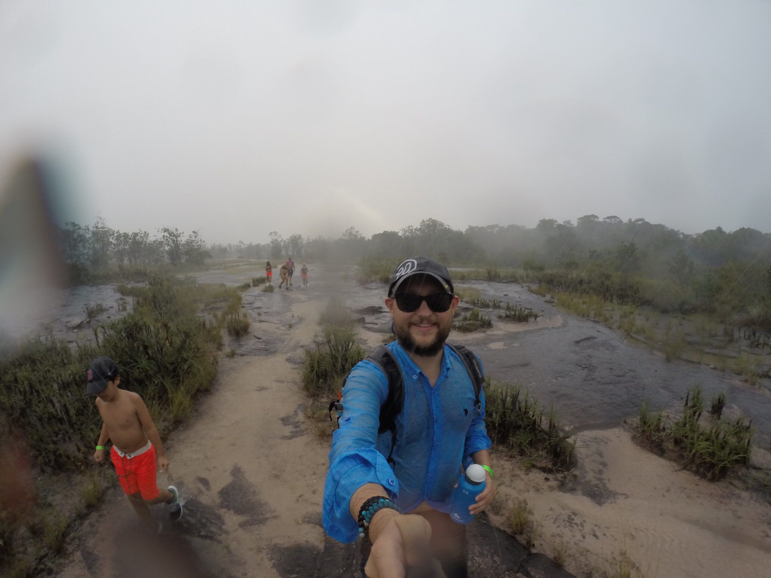 A selfie taken during a trek in Canaima, Venezuela, showing rain starting to fall, small water streams forming, and wet hikers on the trail