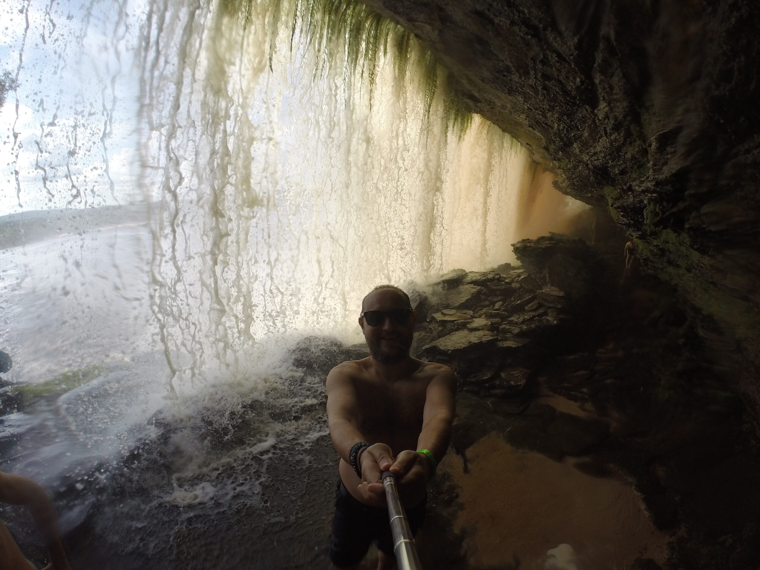 A selfie taken inside a cave behind a waterfall in Canaima, Venezuela, with water cascading down in the background.