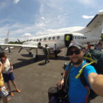 A selfie taken in front of a small plane in Canaima, Venezuela, with passengers disembarking in the background