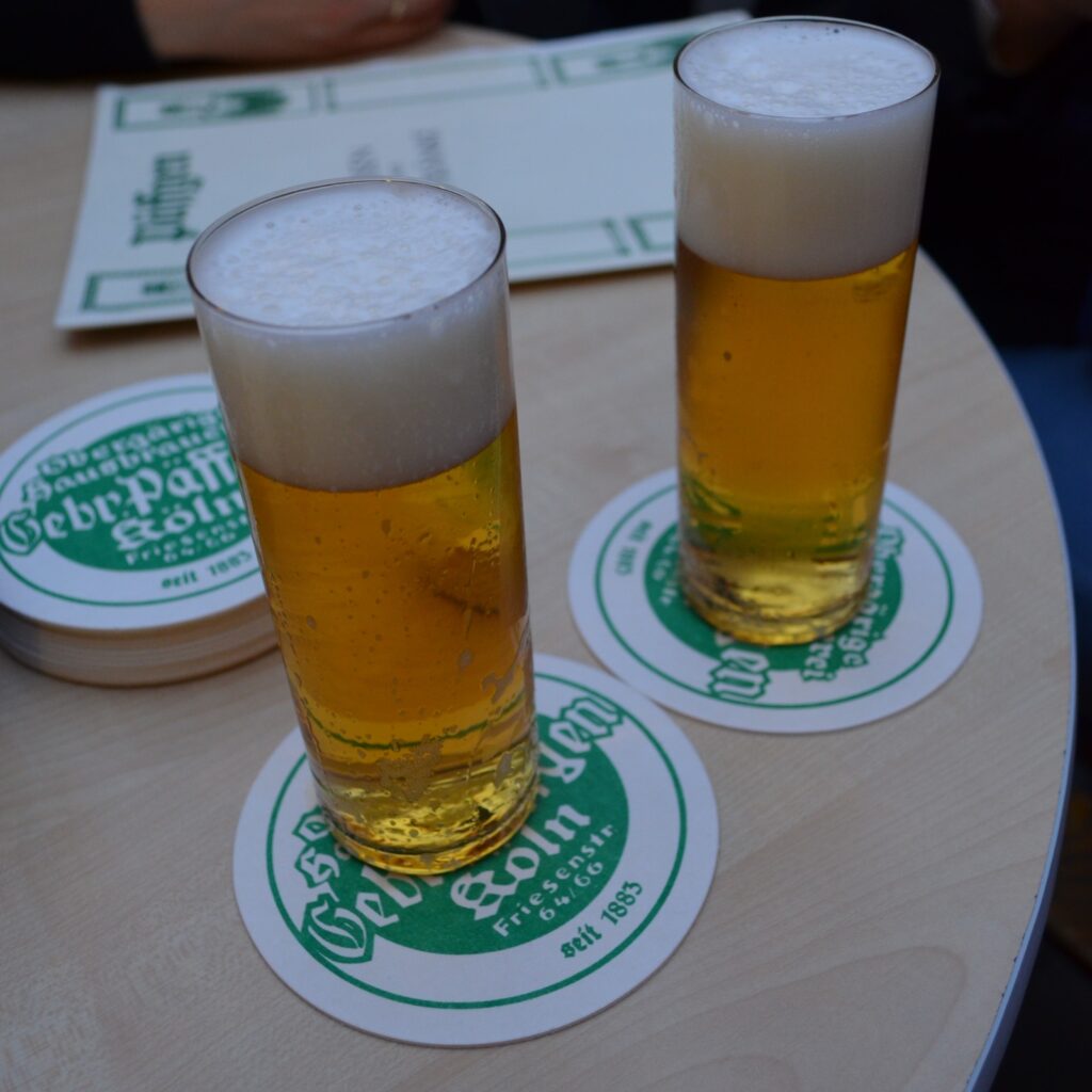 Brauerei Päffgen Cologne 2 Two fresh glasses of Kölsch beer served on branded Päffgen coasters on a wooden table, featured in a guide on where to eat in Cologne.