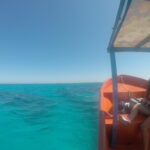 View of La Tortuga Island in the distance from a boat with turquoise calm waters, a couple seated at the front, and a clear blue sky.