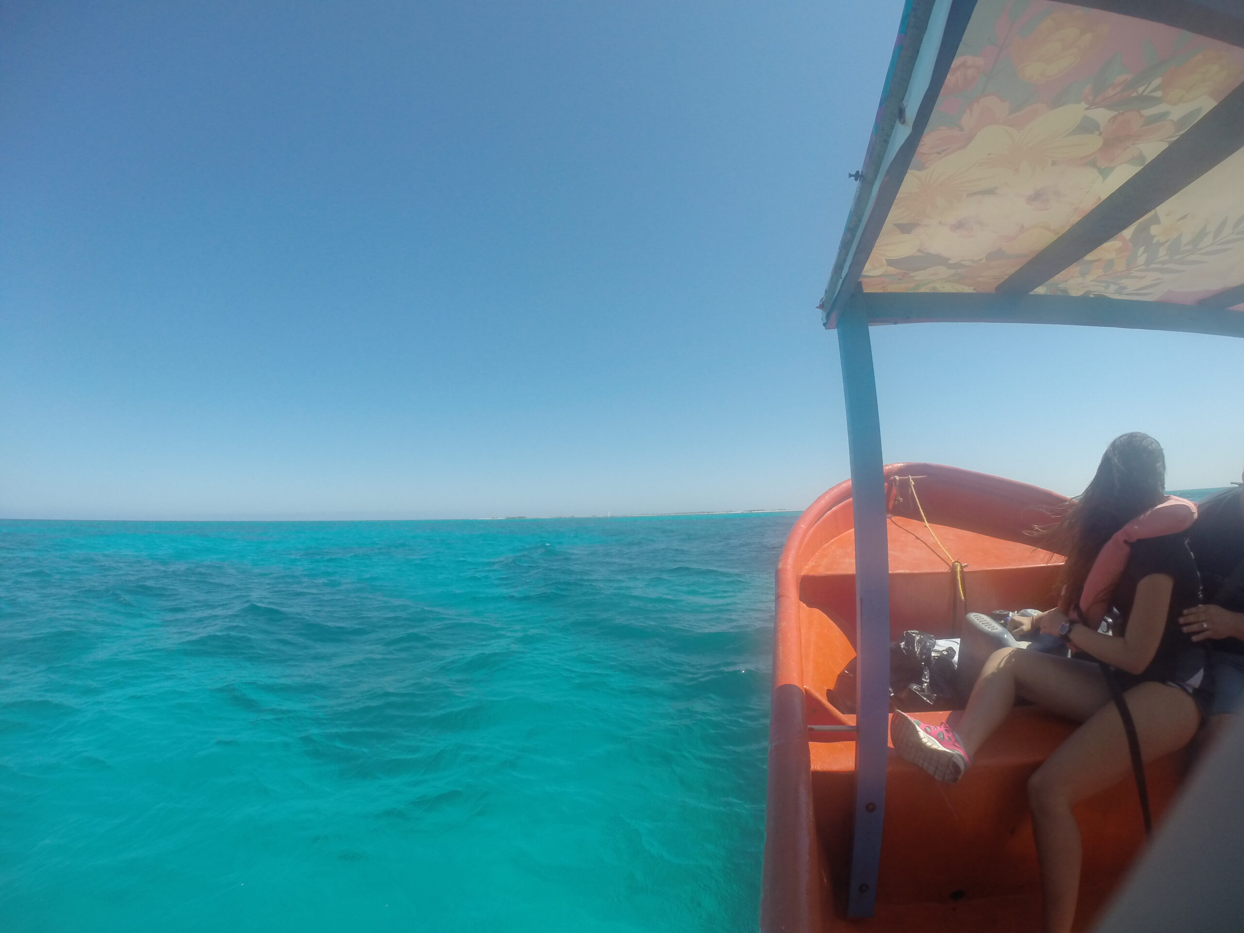 View of La Tortuga Island in the distance from a boat with turquoise calm waters, a couple seated at the front, and a clear blue sky.