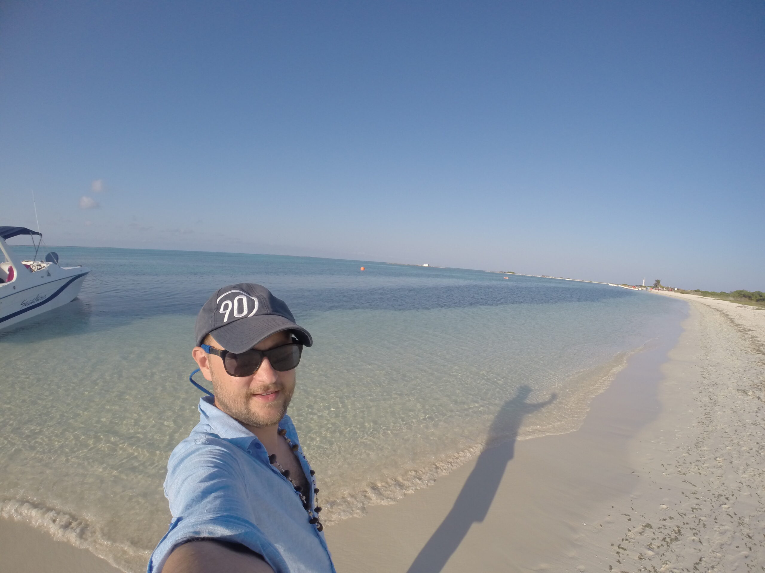 Selfie of a male traveler smiling on a white-sand beach with turquoise water and a clear blue sky on La Tortuga Island, Venezuela.