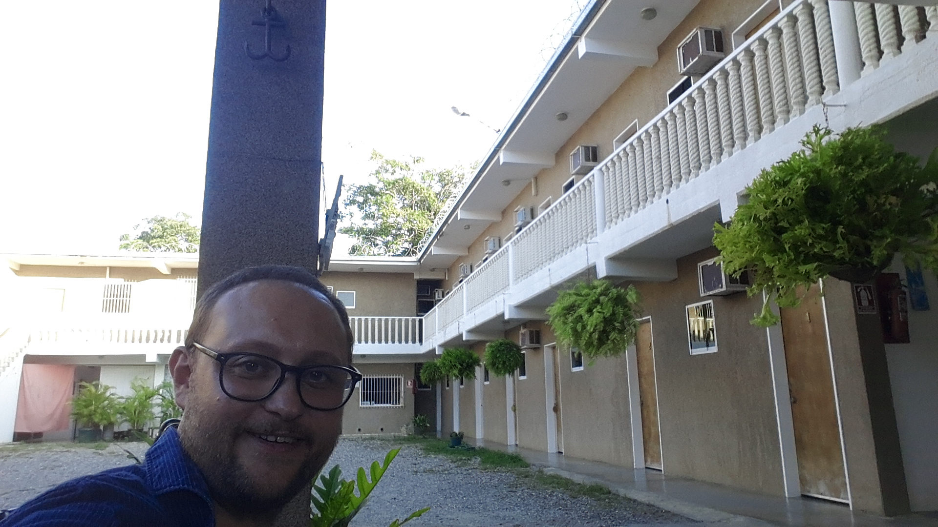 Selfie in front of La Posada de Dorita Hotel courtyard in Higuerote, Venezuela, with hanging plants and two-story rooms.