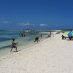 People enjoying a sunny day on the white sandy beach of La Tortuga Island, Venezuela, with turquoise waters and umbrellas.