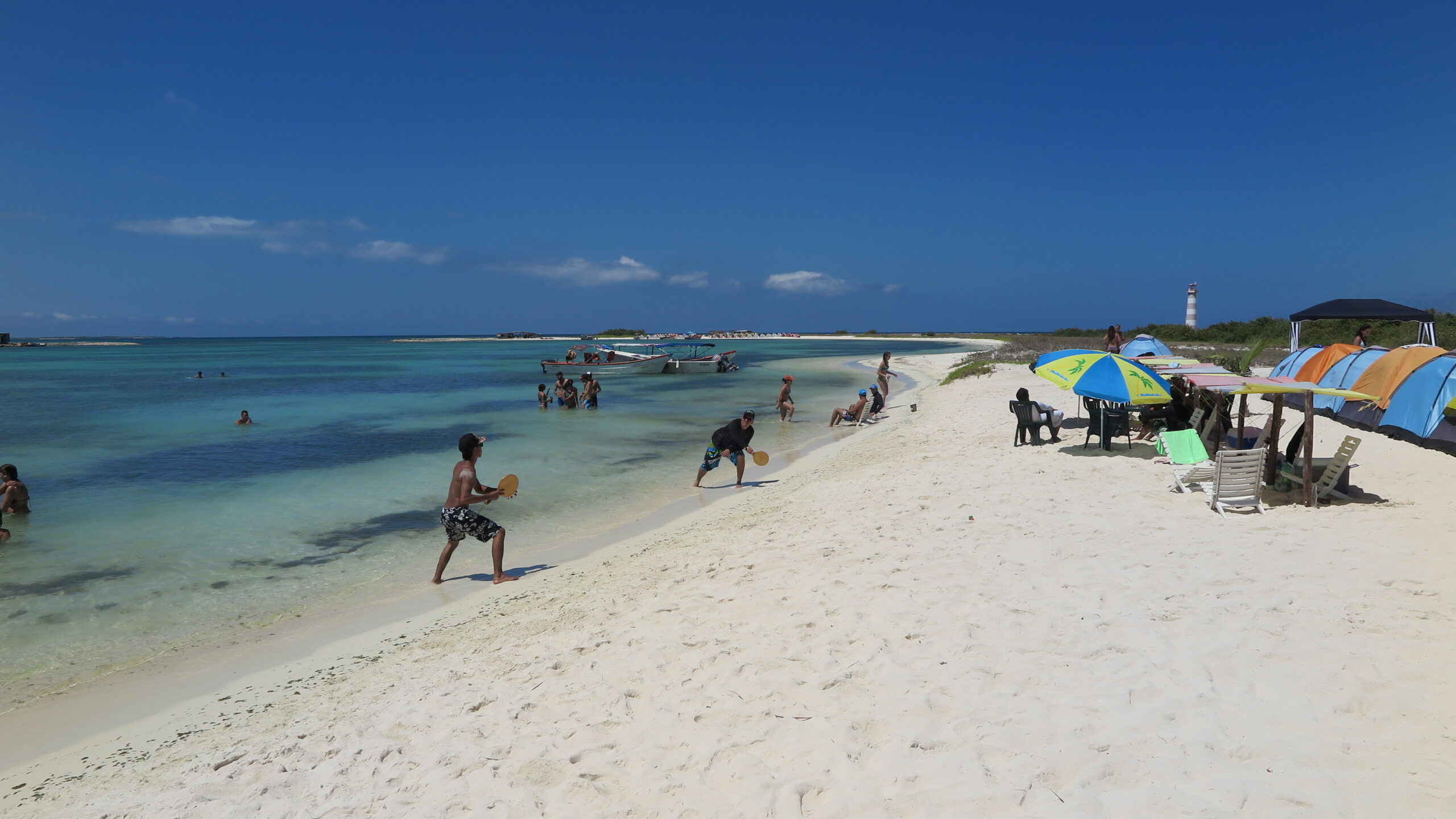 People enjoying a sunny day on the white sandy beach of La Tortuga Island, Venezuela, with turquoise waters and umbrellas.