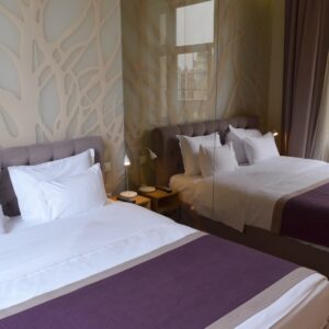 Double bed with white linens, purple throw runner, and mirrored wall detail inside Jump Inn Hotel Belgrade room