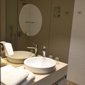 Modern bathroom counter at Jump Inn Hotel Belgrade with vessel sink, circular mirror, and folded white towels