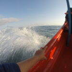 View from a speeding boat from Higuerote to La Tortuga Island, showing ocean waves splashing, a woman seated in front, and the bow lifted by the waves.