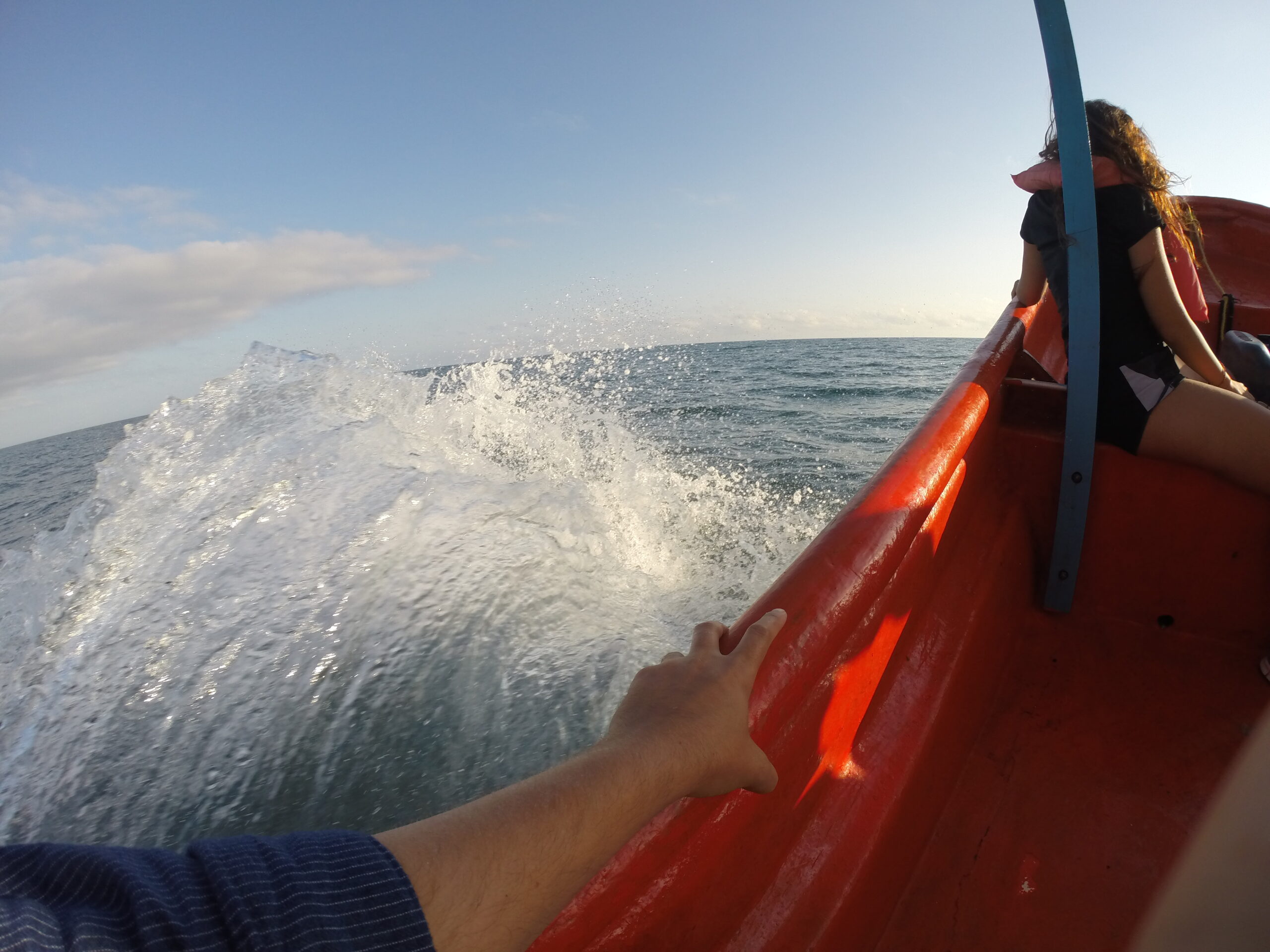 View from a speeding boat from Higuerote to La Tortuga Island, showing ocean waves splashing, a woman seated in front, and the bow lifted by the waves.