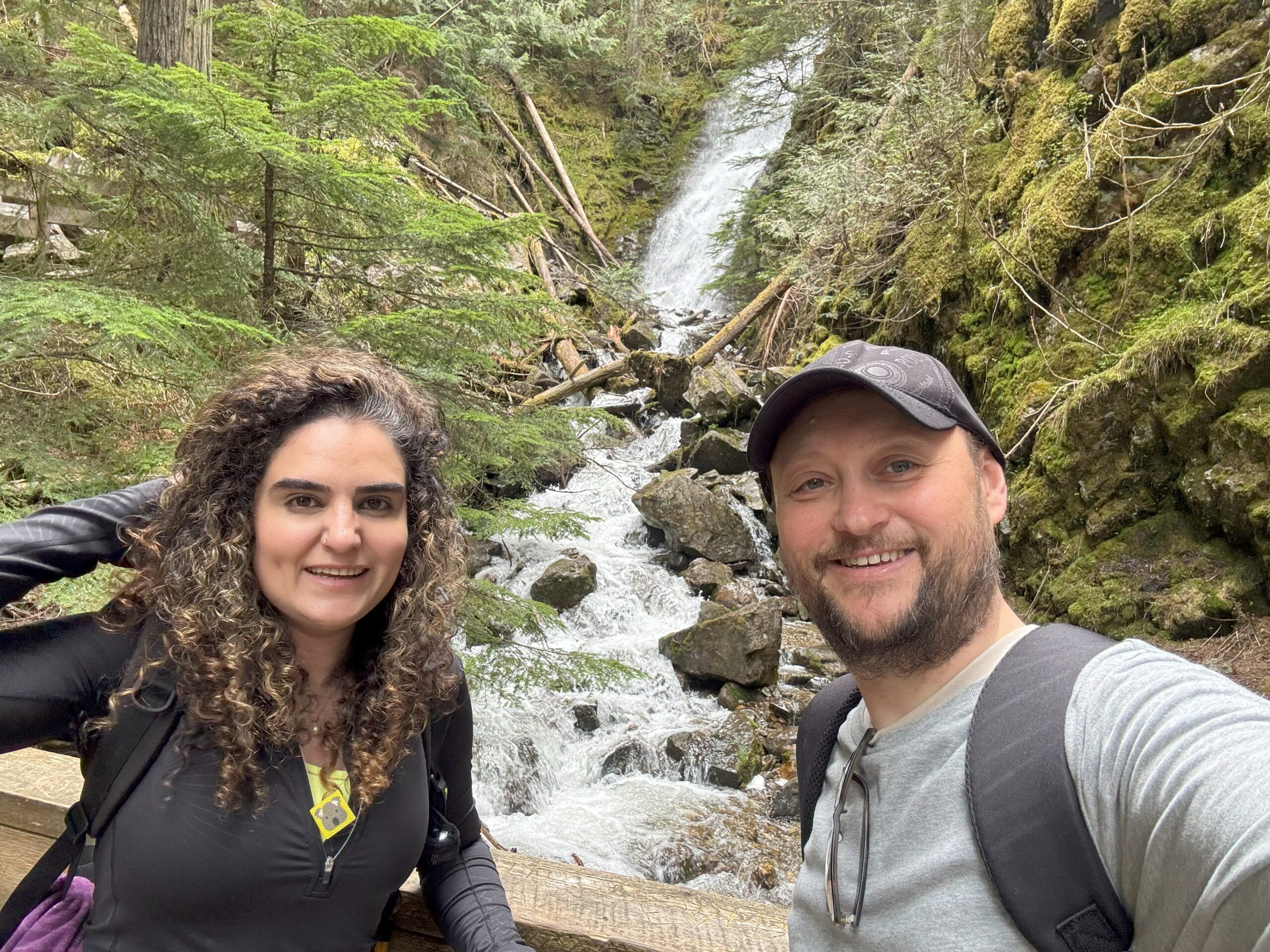 Two people taking a selfie in front of a waterfall in the Ancient Forest.