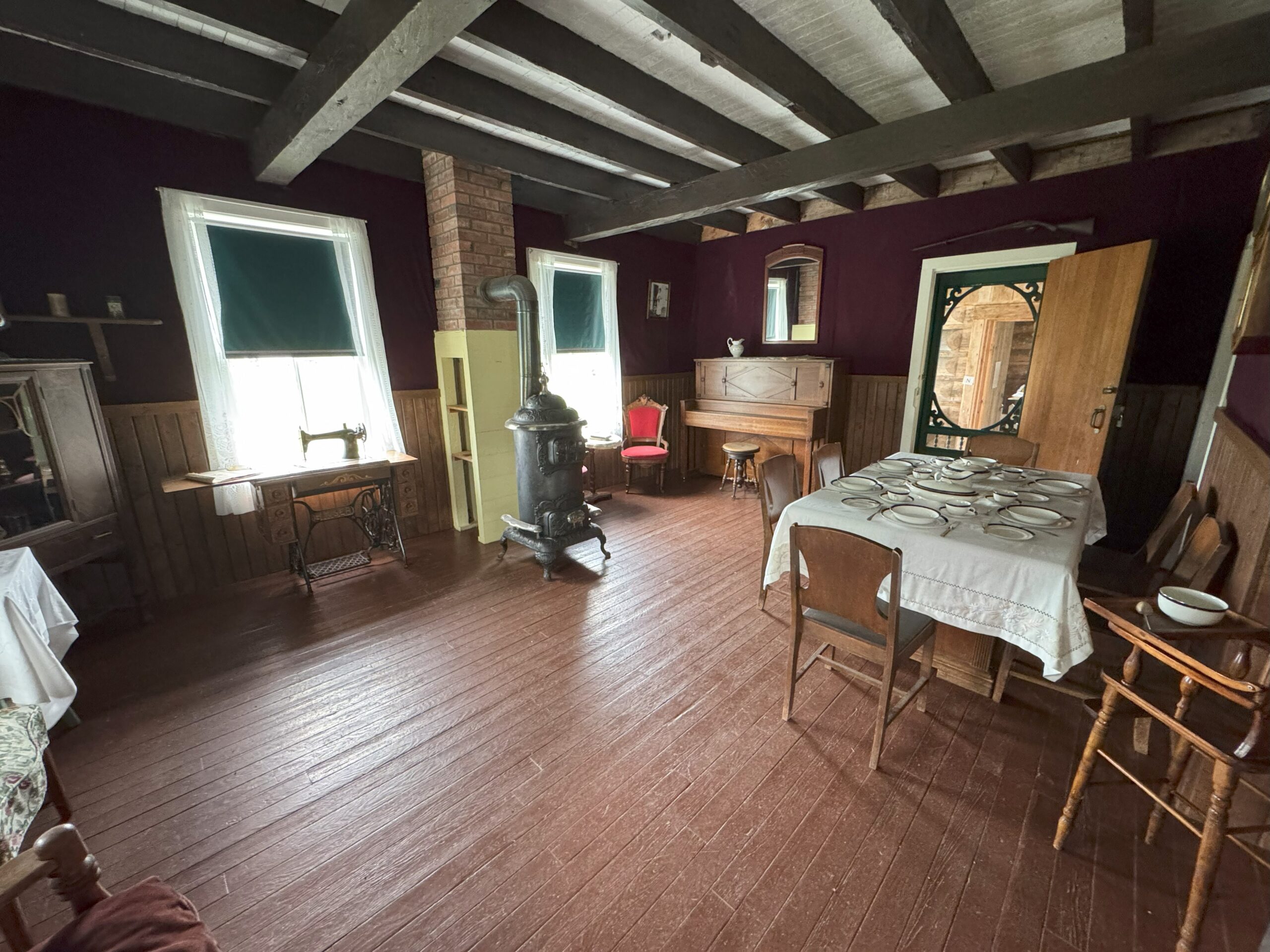 Interior view of the Huble House parlour with antique furniture, a piano, and decorative items.