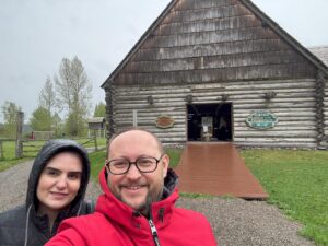 A couple taking a selfie in front of the main entrance to Huble Homestead, a historic site in British Columbia.