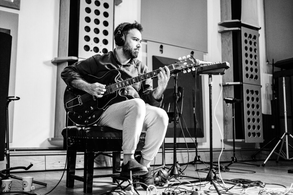 Zenith - Barış Arslan Barış Arslan sits on a bench, playing guitar in a black and white photo taken during the recording of the Zenith jazz album.