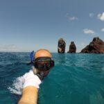 A person snorkeling in the open ocean near striking volcanic rock formations rising from the sea at the Galapagos Islands.