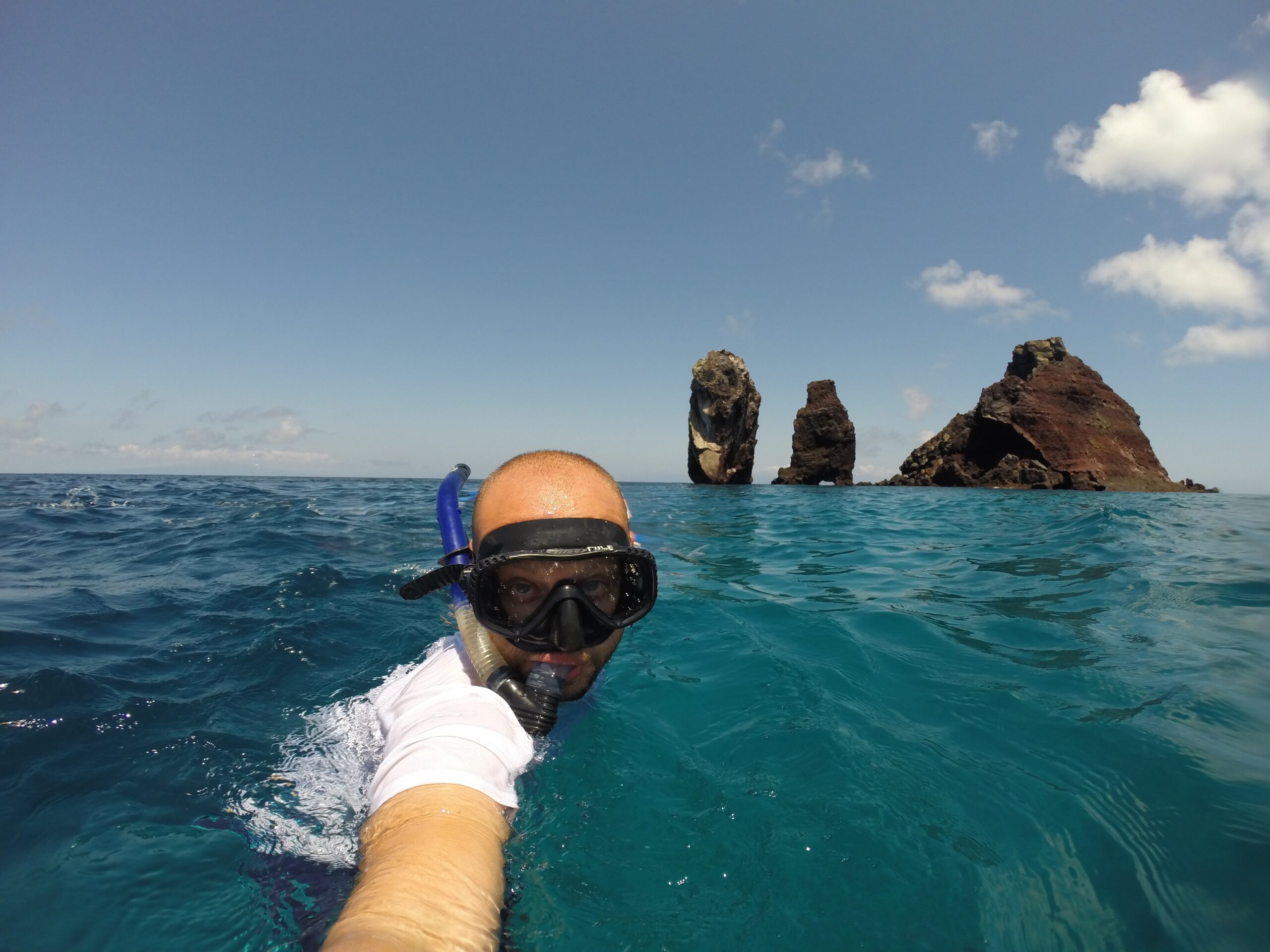 A person snorkeling in the open ocean near striking volcanic rock formations rising from the sea at the Galapagos Islands.