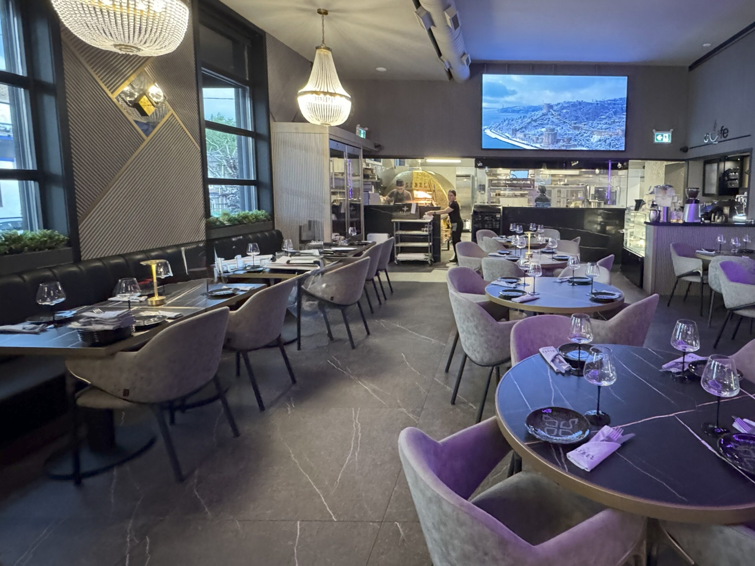 Elegant restaurant interior with modern decor, round and rectangular tables, plush chairs, and dim lighting.