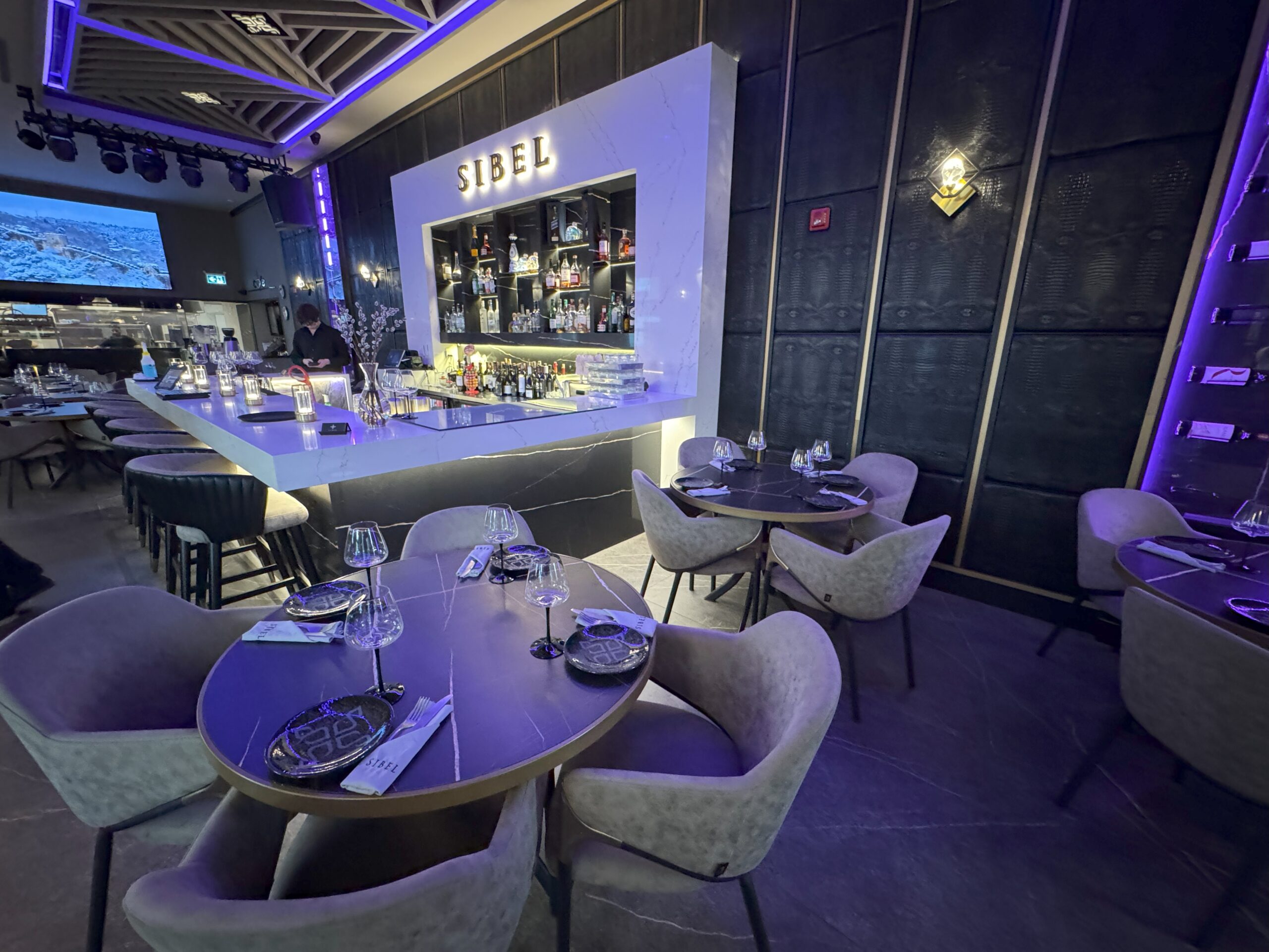 Stylish restaurant bar with modern lighting, marble counter, and surrounding tables set for guests.