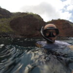 Person wearing a snorkel mask and floating in the ocean near the rugged cliffs of Santa Fe Island, Galapagos.