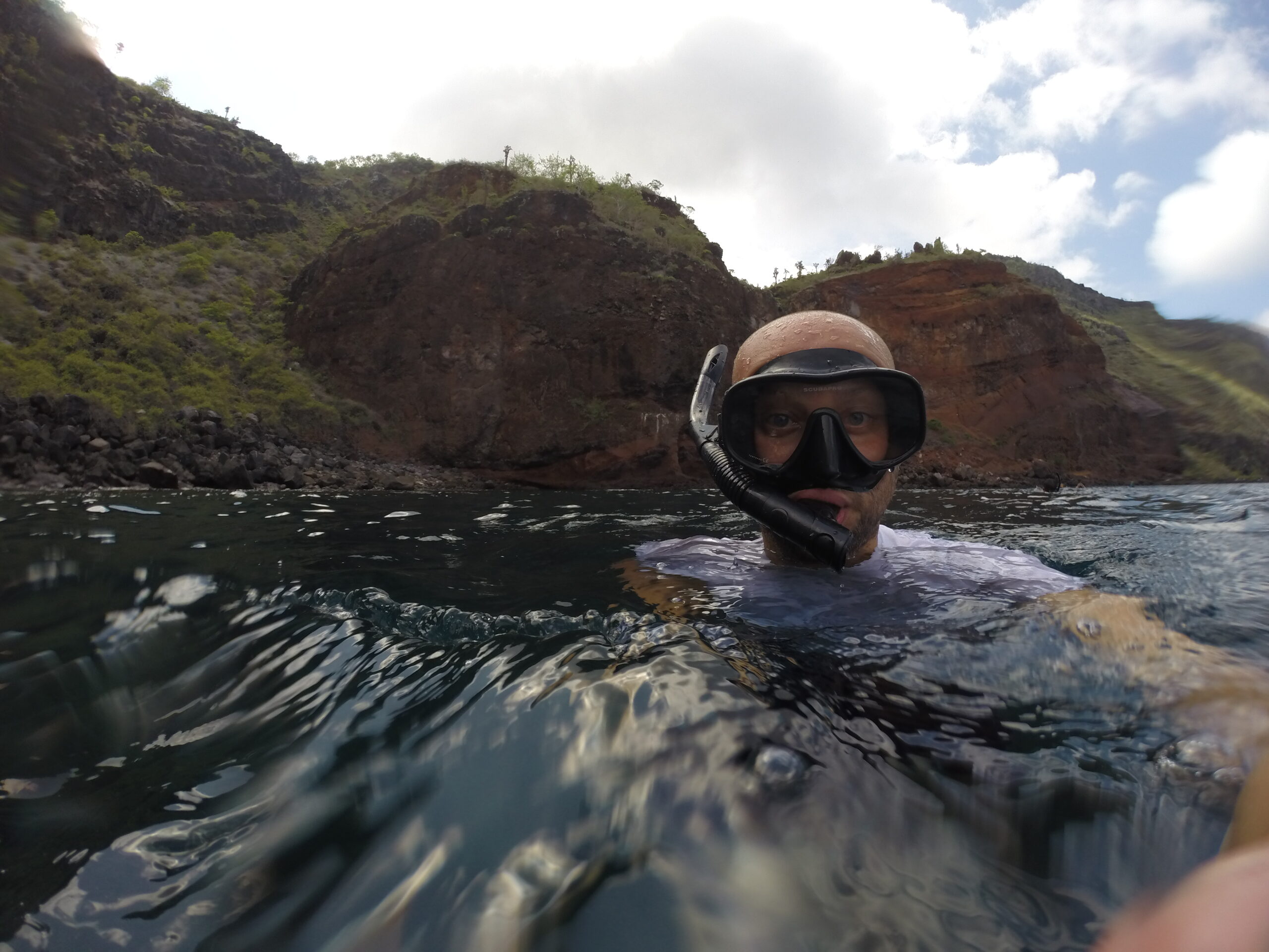 Person wearing a snorkel mask and floating in the ocean near the rugged cliffs of Santa Fe Island, Galapagos.