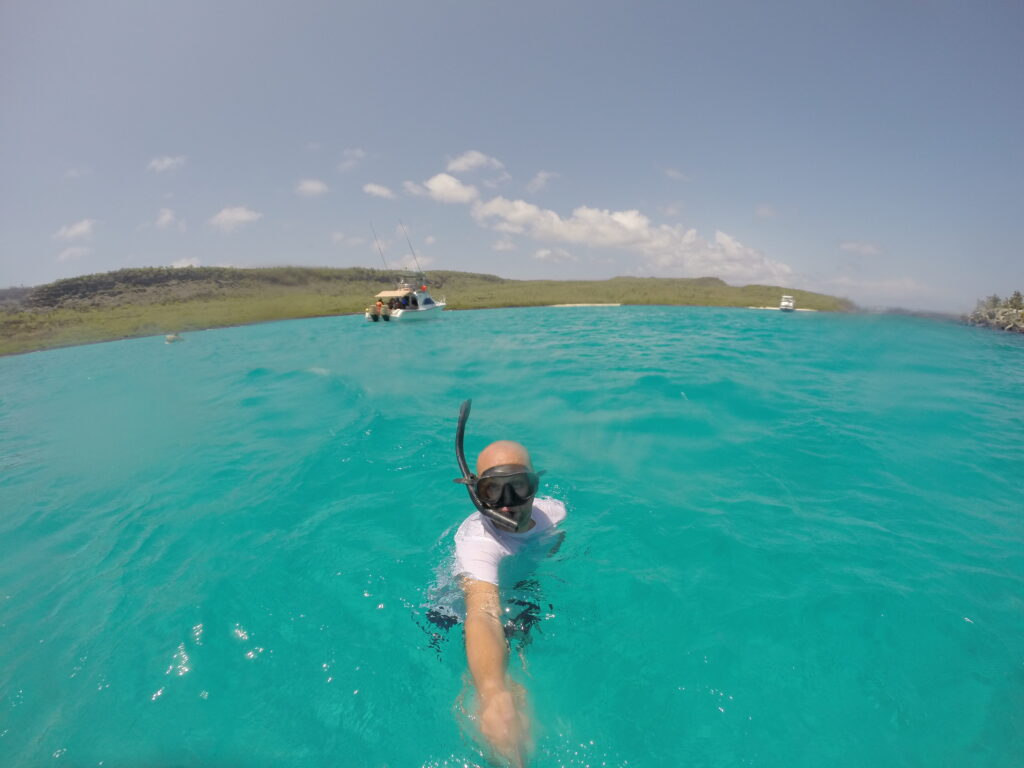 Snorkeling Santa Fe’s turquoise waters A selfie of a snorkeler wearing a mask in the turquoise waters of Santa Fe Island, Galapagos, with a boat visible in the background.