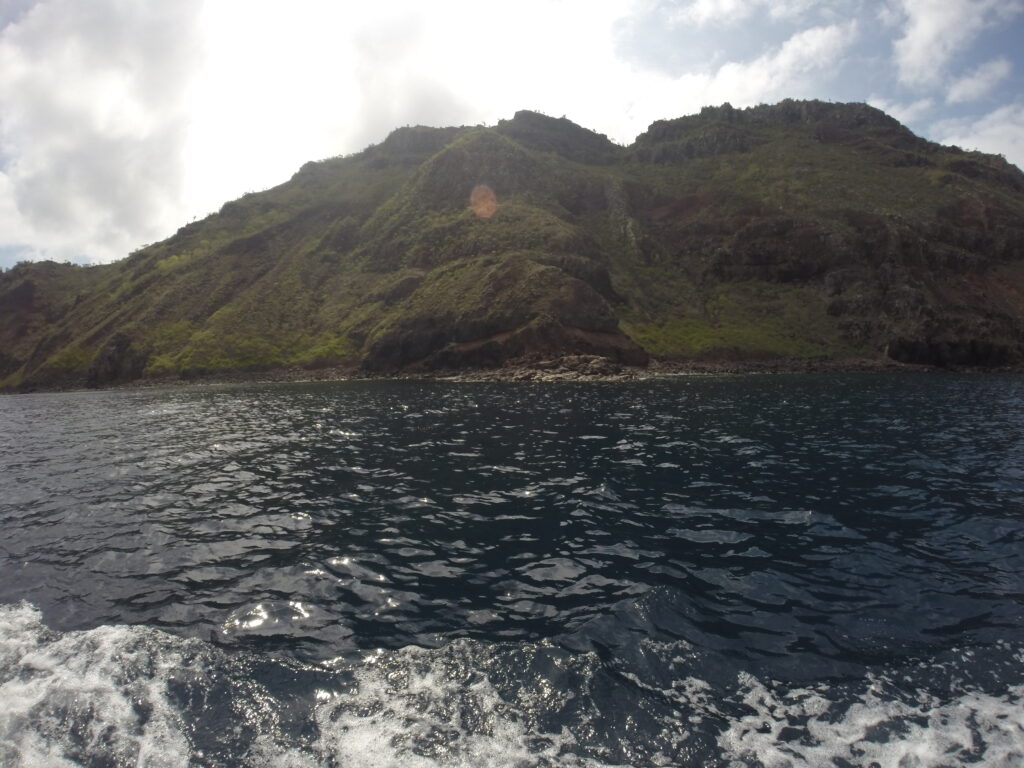 Santa Fe Island Coastal cliffs of Santa Fe Island in the Galapagos, viewed from the ocean under a partly cloudy sky.