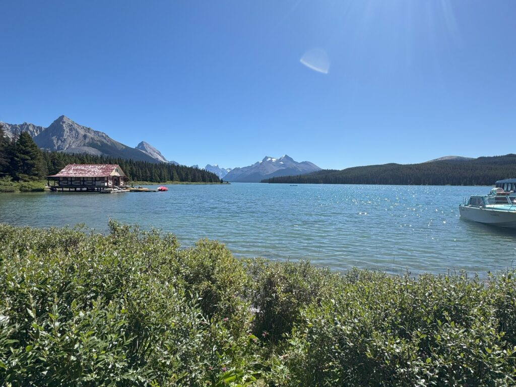 Maligne Lake with its historic red-roofed boathouse, turquoise water, forested shores, and snow-capped mountains in the distance.
