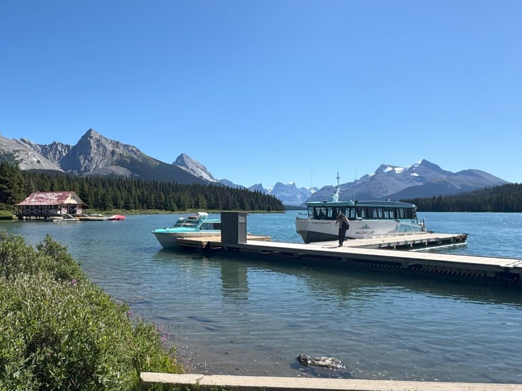 Tour boats docked at Maligne Lake with the historic red-roofed boathouse, turquoise waters, and Rocky Mountain peaks in the background.
