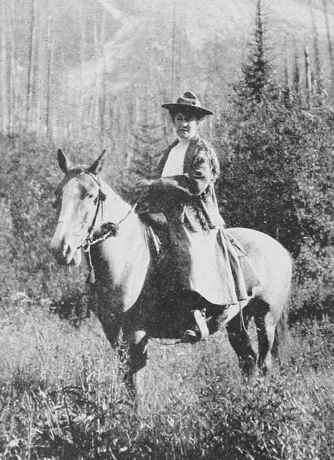 Mary Schäffer Warren on horseback in the Canadian Rockies, early 1900s, surrounded by forest and mountains.
