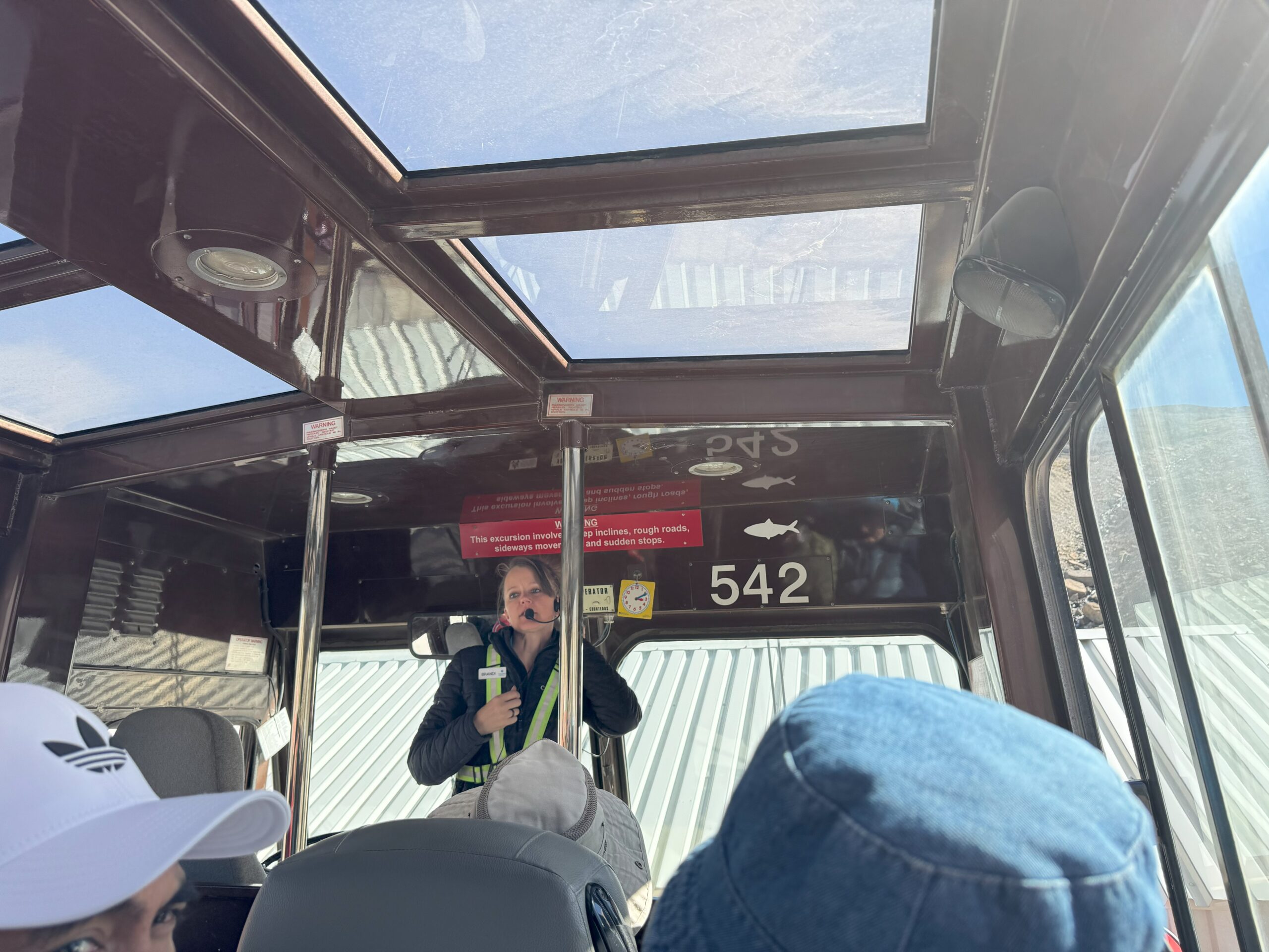 Inside view of an Ice Explorer vehicle with a tour guide speaking into a microphone, surrounded by passengers under a glass roof.