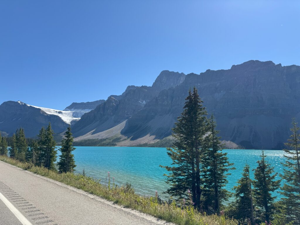 Lake and glacier peaks between Jasper and Banff Turquoise lake surrounded by tall pine trees and rugged mountain peaks between Jasper and Banff on a sunny day.