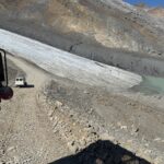 Athabasca Buzulu'na doğru dik ve kayalık bir yoldan inen bir Ice Explorer aracının görüntüsü. İleride başka bir buzul aracı ve buzun yanında görünen bir eriyik su gölü.