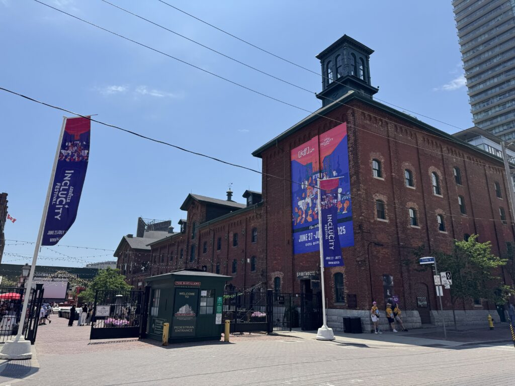 Historic red-brick buildings at Toronto’s Distillery District on a sunny day, decorated with banners for the InCluCity Festival.