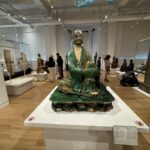 A glazed ceramic statue of a seated monk in a green robe on display at the Royal Ontario Museum’s Asian art gallery.
