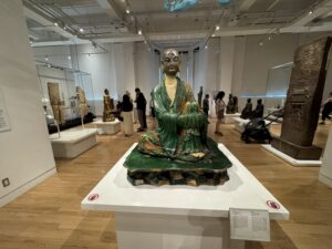 A glazed ceramic statue of a seated monk in a green robe on display at the Royal Ontario Museum’s Asian art gallery.