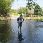 Venezuela Chuao köyünde, tropikal doğa ve köy manzarası arasında sığ bir nehirde duran bir kişi.