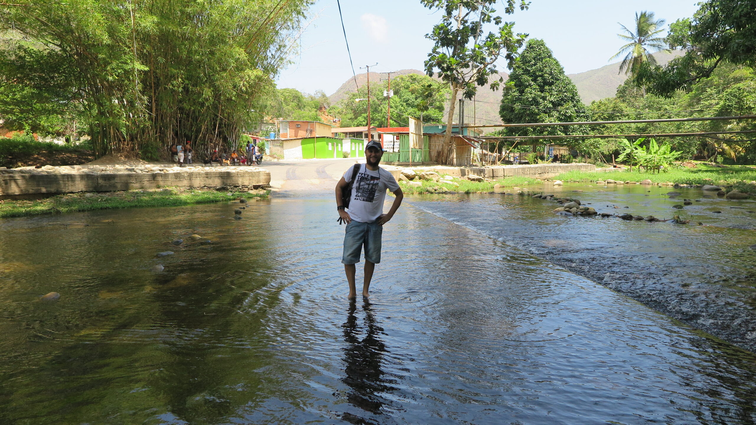 Venezuela Chuao köyünde, tropikal doğa ve köy manzarası arasında sığ bir nehirde duran bir kişi.