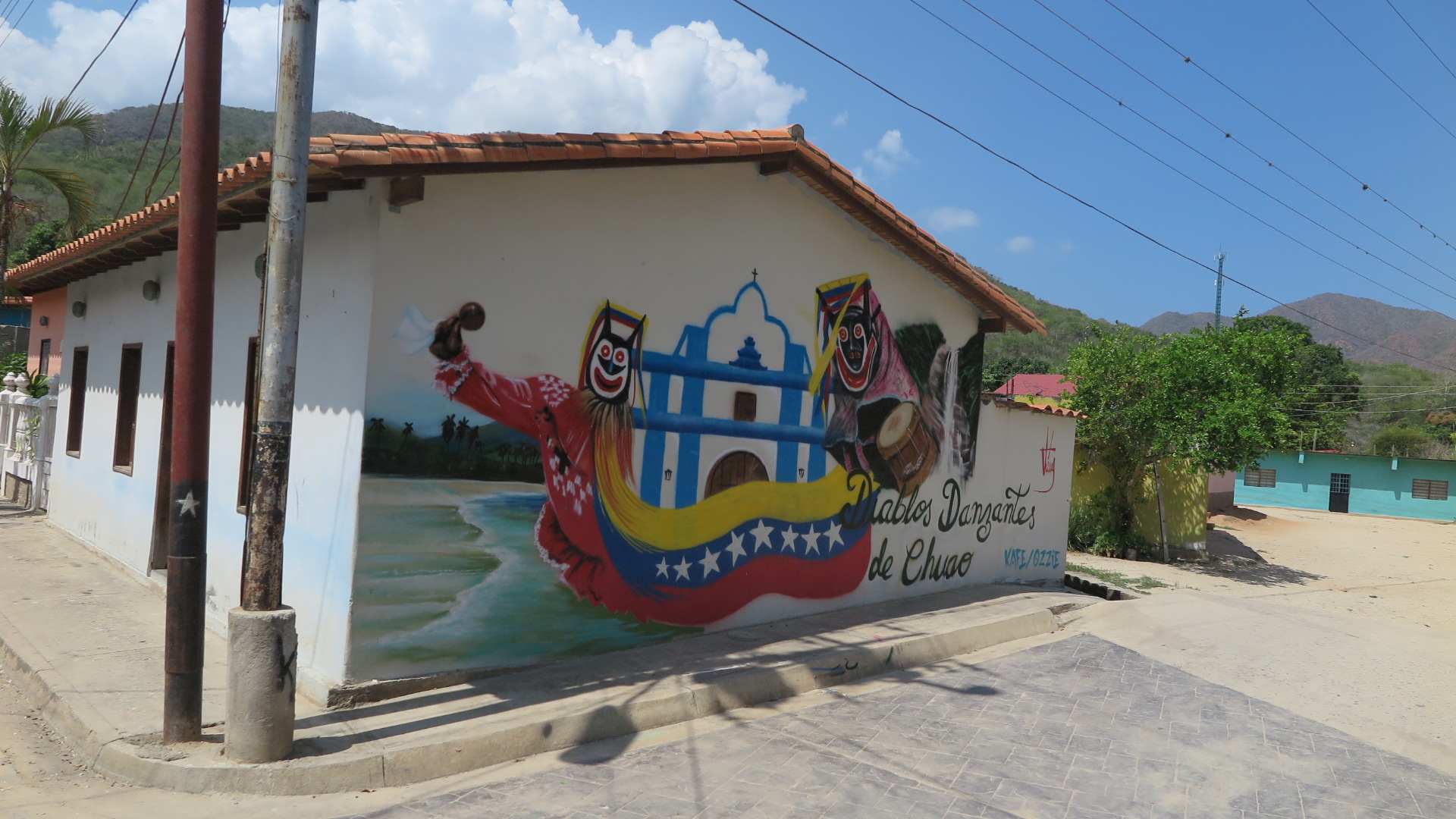 Venezuela'nın Chuao köyünde, beyaz bir binanın üzerinde "Diablos Danzantes de Chuao" (Chuao Dans Eden Şeytanlar) geleneğini, köy kilisesini ve Venezuela bayrağını tasvir eden renkli bir duvar resmi.