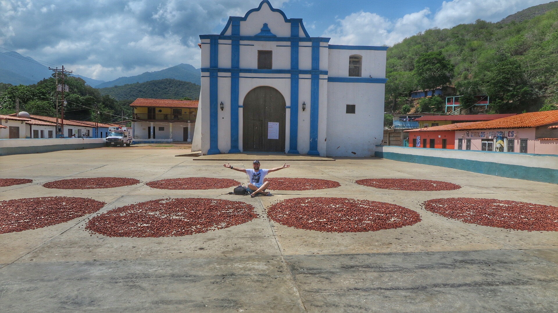 Venezuela'daki tarihi beyaz ve mavi renkli Iglesia de la Inmaculada Concepción kilisesinin önünde, kurumaya bırakılmış kakao çekirdekleri halkalarının arasında oturan bir gezgin.