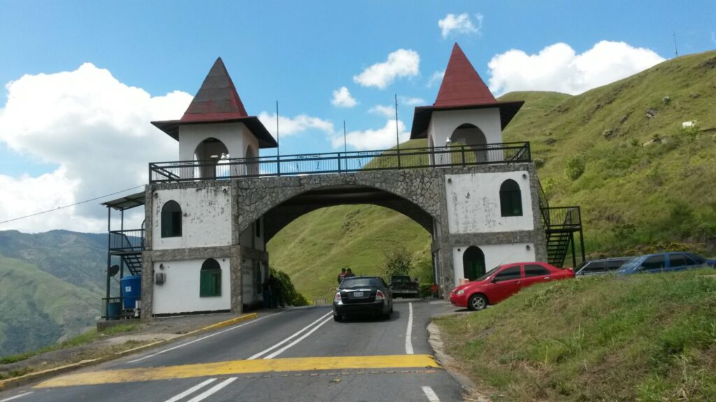 Colonia Tovar The Gate Scenic entrance gate with twin towers on the road to Colonia Tovar, Venezuela, surrounded by green mountains under a bright blue sky.