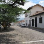 A cobblestone street in Girón, Colombia, with white colonial buildings and students in uniforms.