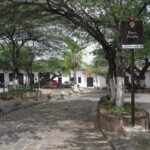 Plaza Peralta in Girón, a quiet square with leafy trees and a brown information sign.