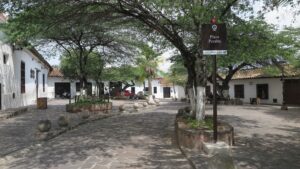 Girón'da Plaza Peralta; yapraklı ağaçlar ve kahverengi bir bilgi tabelasının bulunduğu sakin bir meydan.