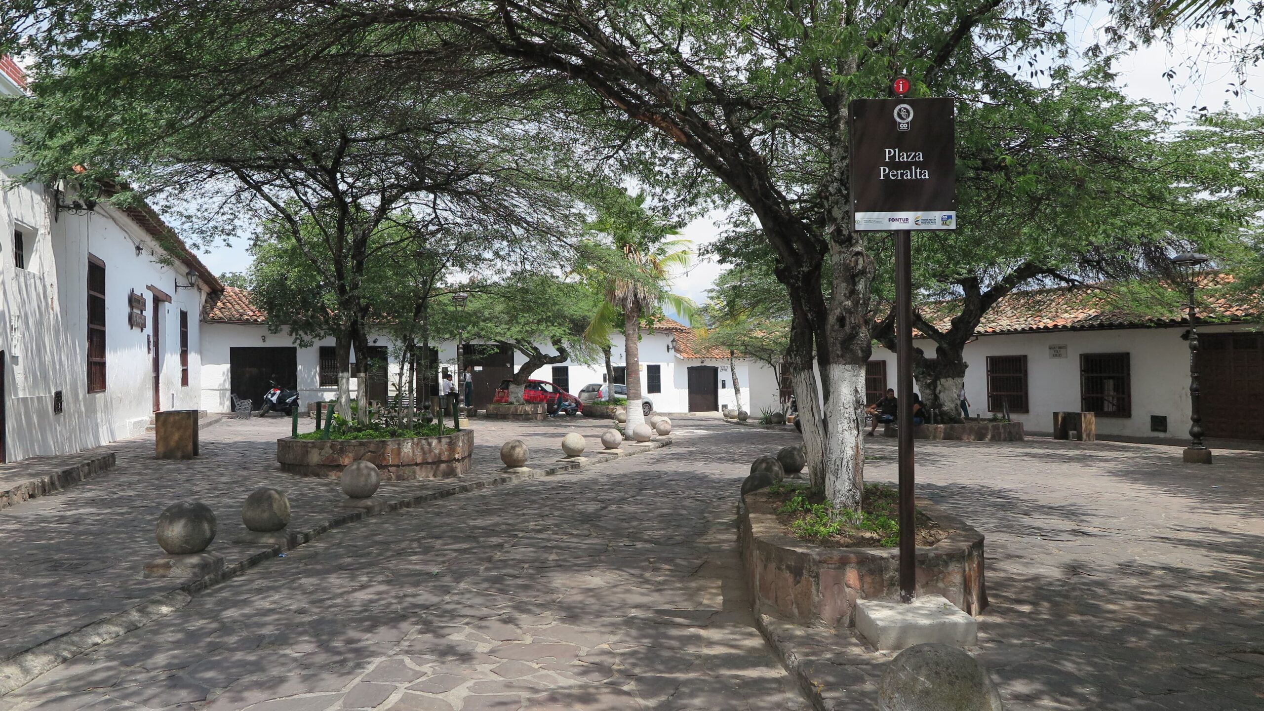 Plaza Peralta in Girón, a quiet square with leafy trees and a brown information sign.