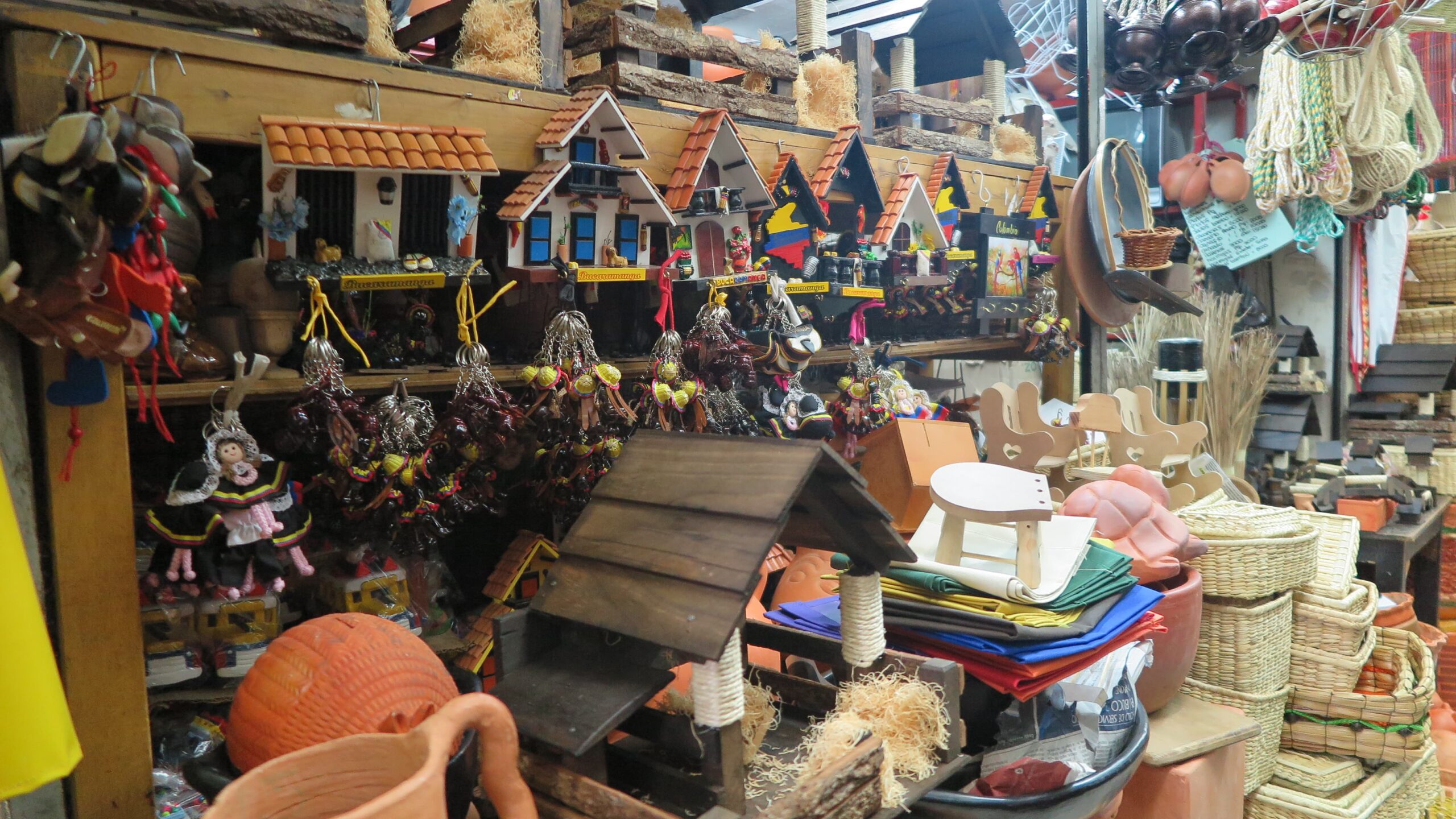 Colorful miniature Colombian house magnets and handcrafted wooden souvenirs on a display shelf at Plaza Central market in Bucaramanga.