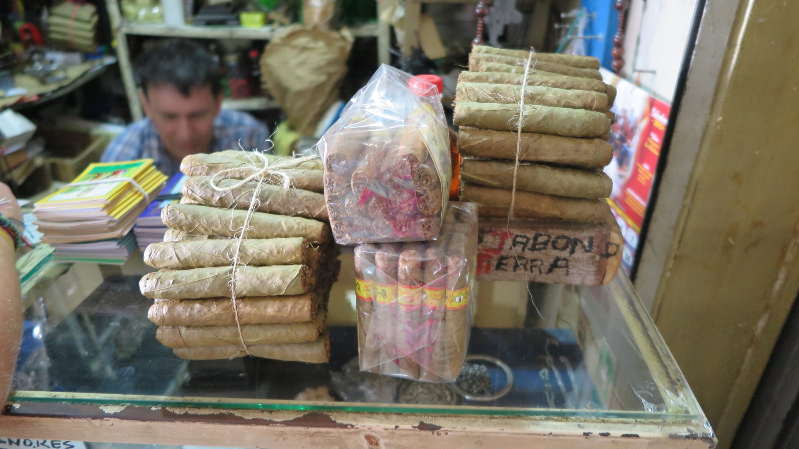 Hand-rolled Colombian cigars tied with string and packaged in plastic on a glass counter at Plaza Central market.