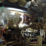 A variety of handcrafted wicker baskets and woven birdcages hanging in a dim market stall.