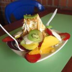 Bucaramanga'daki bir pazar tezgahında mango, çilek, kivi, peynir ve gofret ile beyaz tabakta servis edilen canlı bir Kolombiya meyve salatası (Ensalada de Frutas).