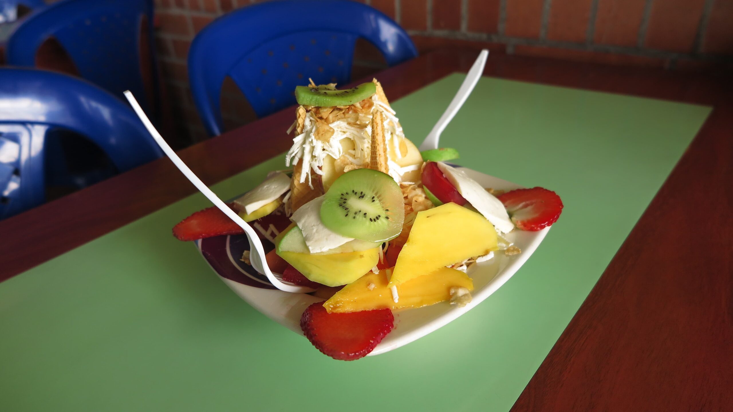 Bucaramanga'daki bir pazar tezgahında mango, çilek, kivi, peynir ve gofret ile beyaz tabakta servis edilen canlı bir Kolombiya meyve salatası (Ensalada de Frutas).