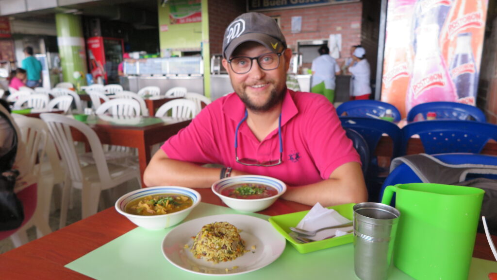 Kolombiya, Bucaramanga'daki Plaza Central pazarının yemek katında, önünde geleneksel Kolombiya yemekleri olan bir masada outran bir adam.